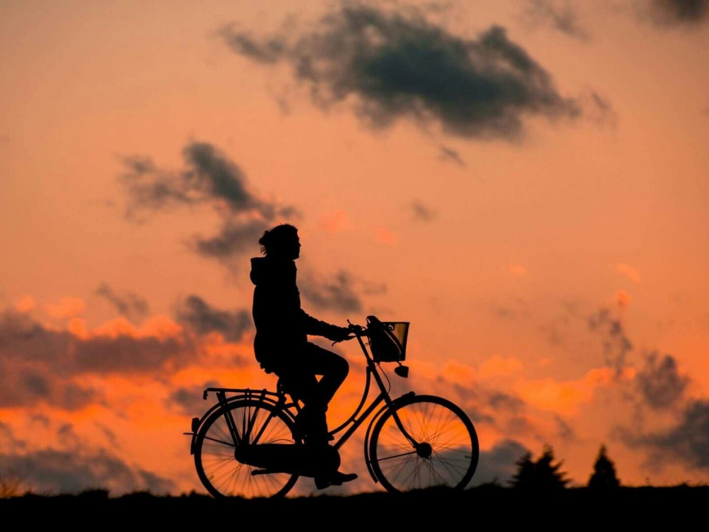 a woman riding a bicycle while the sun sets behind her