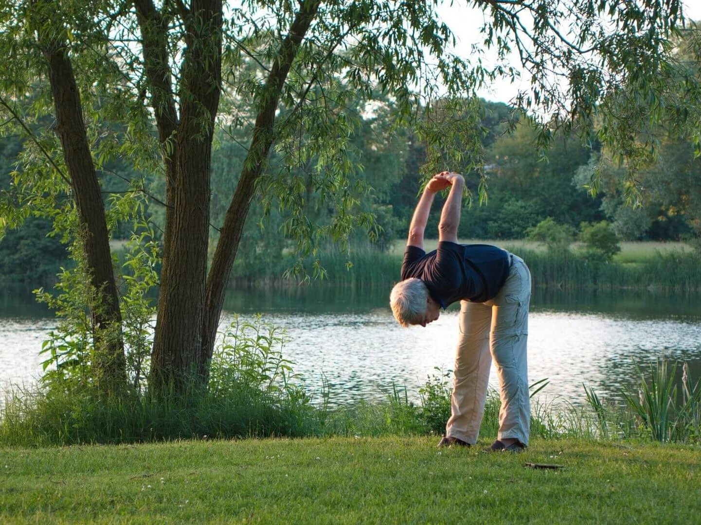 older man doing stretches by the lakeside